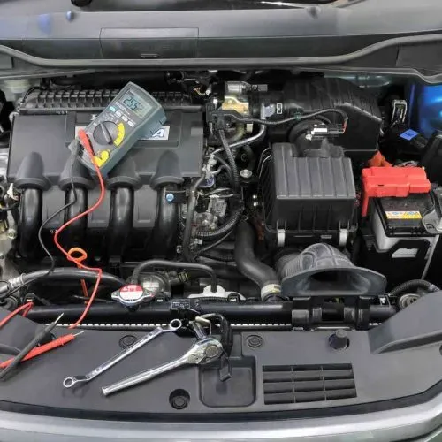 Car engine compartment with tools and a multimeter.